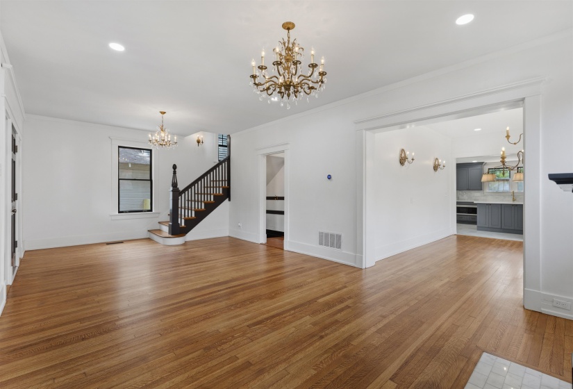 Hardwood flooring throughout the main living space featuring a grand staircase with dark wood newel post and balusters