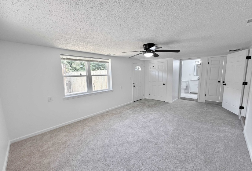 Spacious room featuring light gray carpeting, a multi-pane window, a ceiling fan with integrated lighting, and white paneled doors