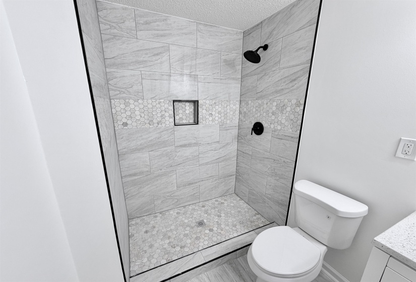 Walk-in shower featuring light grey tile walls, a decorative hexagonal tile band, and a hexagonal tile floor