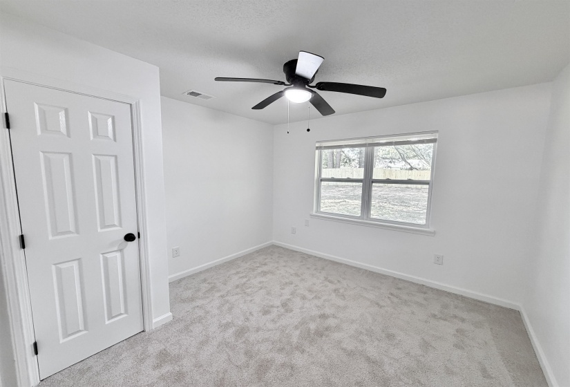 Light gray carpeting with white baseboards, a white paneled door with black hardware, a black ceiling fan with integrated lighting, and a window with white trim