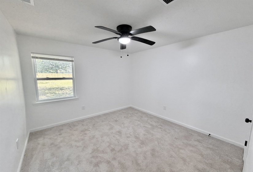 Bright room featuring light gray carpet, white walls, a single window with white trim, and a black ceiling fan with an integrated light fixture