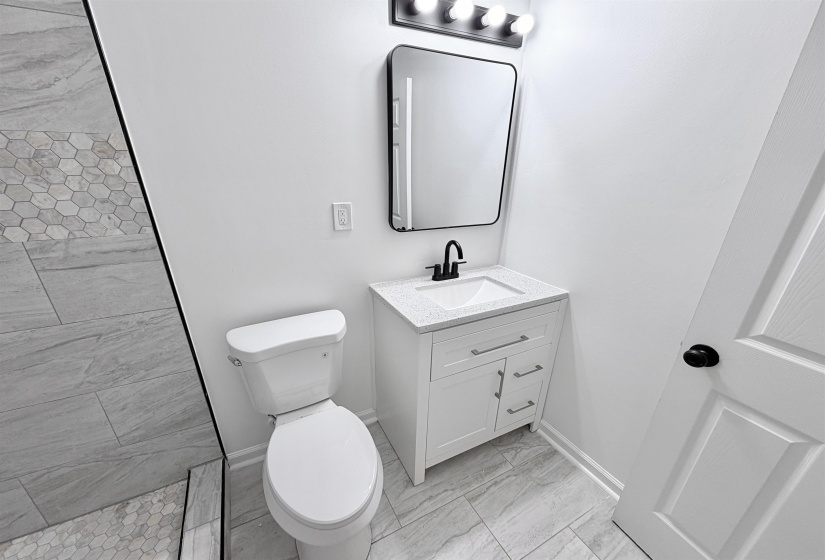Bathroom featuring a white vanity with integrated sink, a dark framed mirror, and a four-bulb vanity light fixture