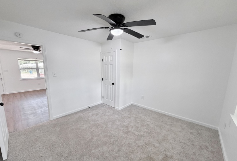 Bedroom featuring light gray carpet flooring, white walls, a black ceiling fan with integrated lighting, and a white paneled door with black hardware