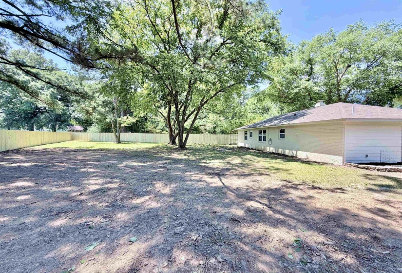 Expansive outdoor area featuring a new wood privacy fence, mature trees, and a partial lawn