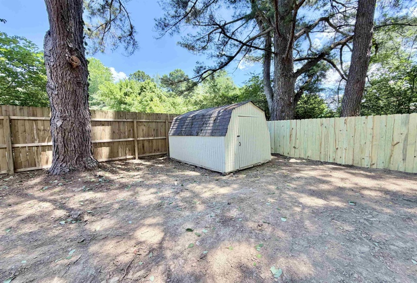 Backyard area featuring a wooden storage shed with a gambrel roof, bordered by a wood privacy fence