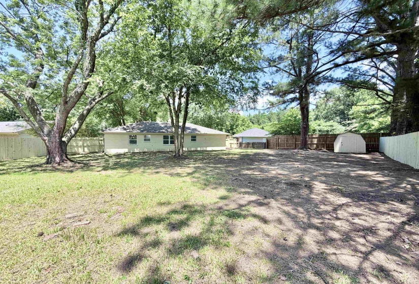 Expansive backyard featuring a partial grass lawn, mature trees, wood privacy fencing, and a detached storage shed