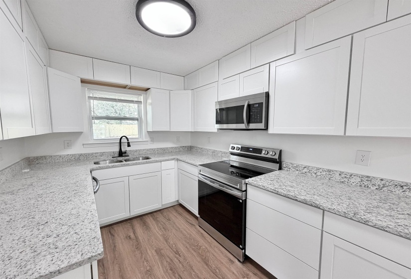 Modern kitchen featuring abundant white cabinetry, stainless steel appliances, speckled countertops, and wood-finish flooring