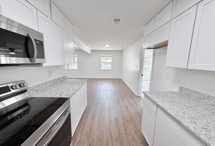 Modern kitchen featuring white shaker cabinetry, stainless steel appliances including a built-in microwave and electric range, and light-colored speckled countertops