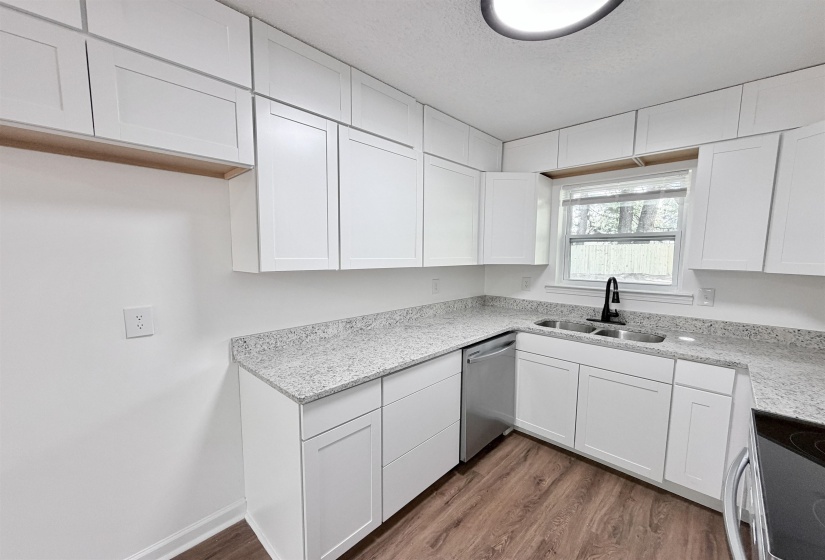 Kitchen featuring white shaker-style cabinetry, light speckled countertops, and wood-finish flooring