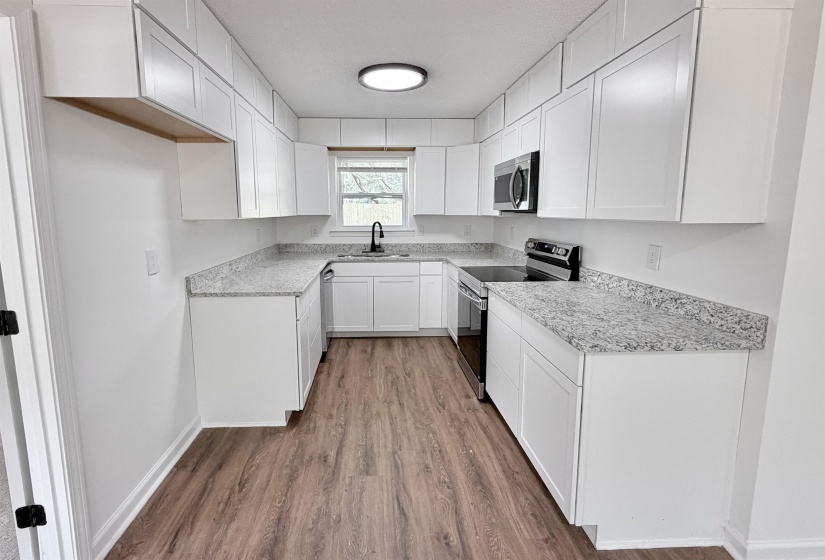 U-shaped kitchen featuring white shaker cabinetry, speckled countertops, stainless steel appliances, wood-finish flooring, and a contemporary ceiling light fixture