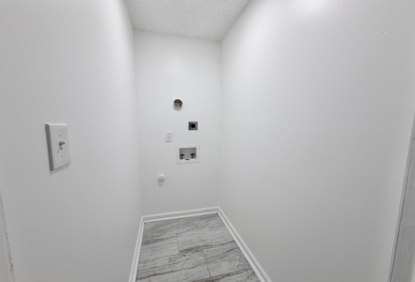 Dedicated laundry space featuring tile-pattern flooring, white baseboards, and essential utility hookups