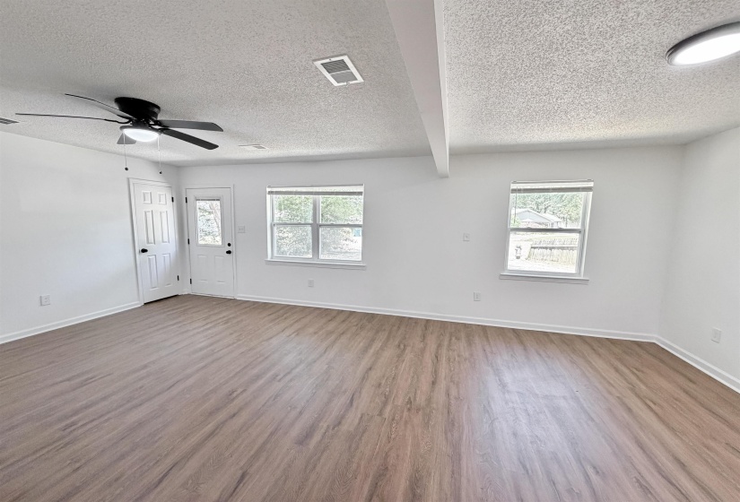 Spacious room featuring wood-finish flooring, white walls, and multiple windows providing natural light