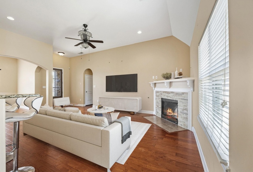 Living area featuring wood-finish flooring, a stone-clad fireplace with a decorative mantel, and arched doorways