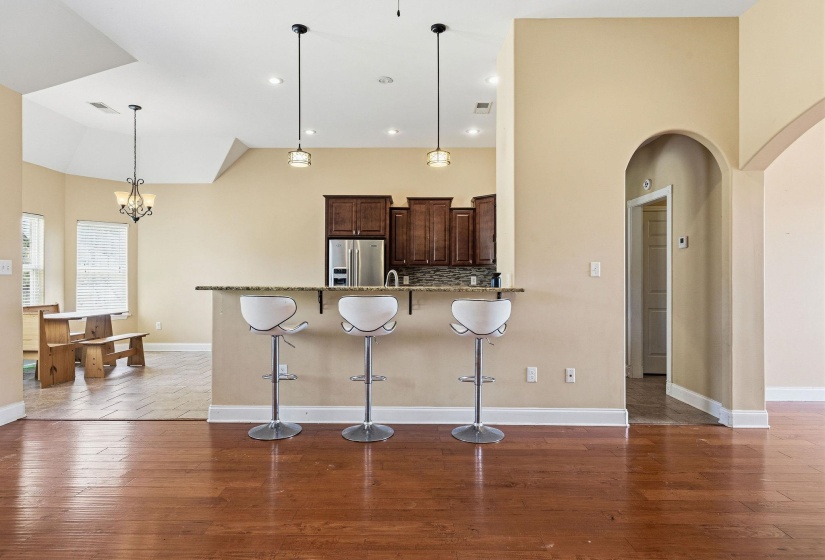 Open concept interior featuring wood-finish flooring, a kitchen bar with pendant lighting, dark wood cabinetry, and stainless steel appliances