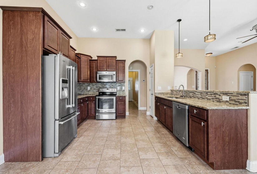 Kitchen featuring dark wood cabinetry, stainless steel appliances, granite countertops, and a mosaic tile backsplash