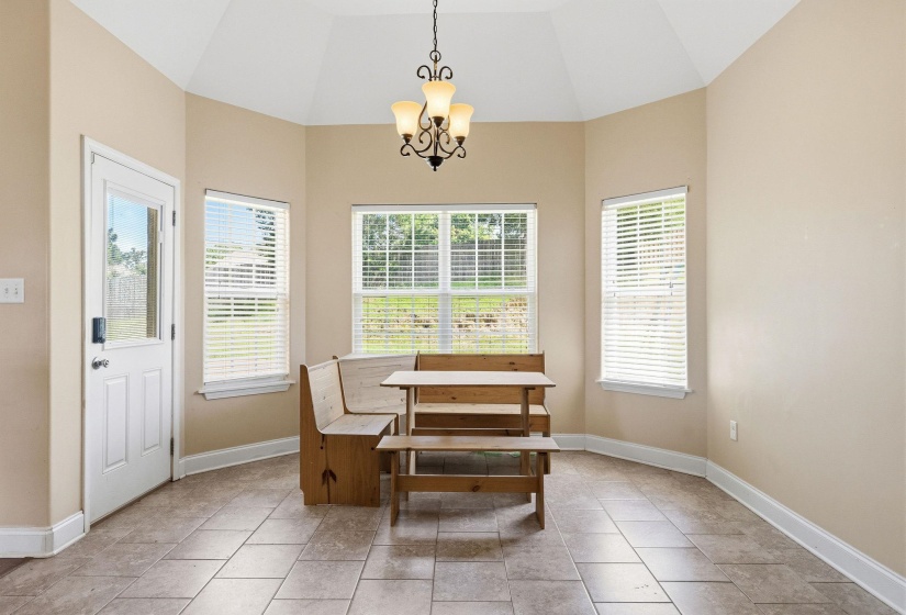 Dining area featuring a vaulted ceiling with an ornamental chandelier, multiple windows with blinds, and tile flooring