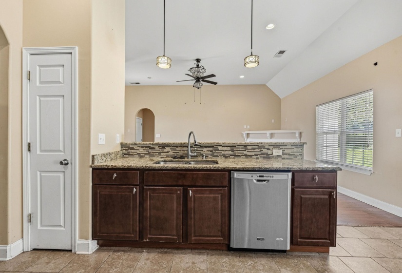 Kitchen island with granite countertop, undermount sink, stainless steel dishwasher, and mosaic tile backsplash