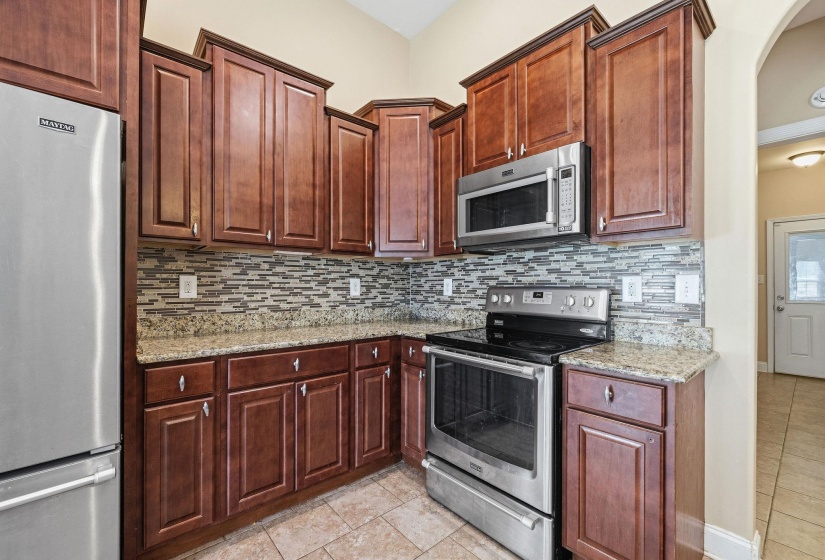 Kitchen featuring wood cabinetry, stainless steel appliances, granite countertops, tile backsplash, and tile flooring