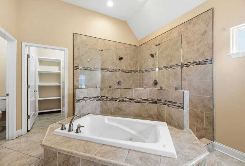Spacious bathroom featuring a built-in jetted tub, tiled surround, and expansive walk-in shower with glass panels