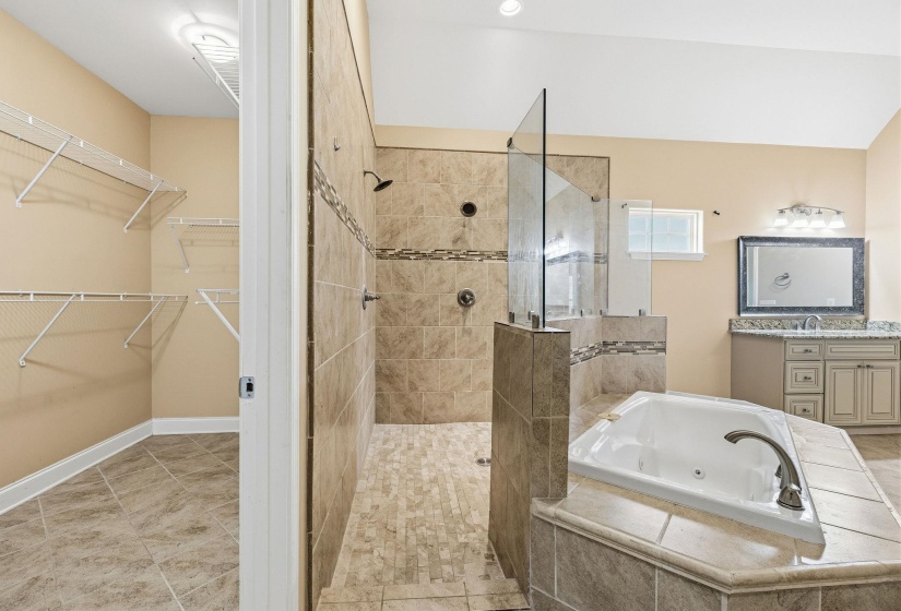 Bathroom featuring a walk-in shower with dual shower heads, a built-in jetted tub, a single vanity with granite-style countertop, and an adjacent closet with wire shelving