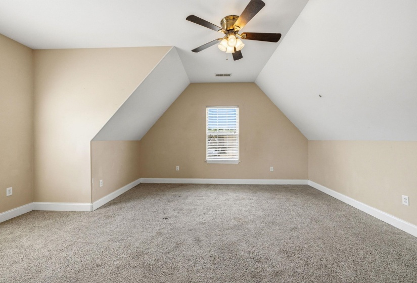Carpeted room featuring an angled ceiling, a window with blinds, a ceiling fan with integrated lighting, and neutral wall tones