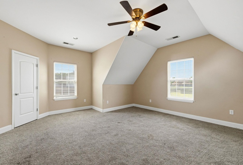 Spacious room featuring sloped ceilings, two bright windows with blinds, a ceiling fan with integrated lighting, and neutral-toned wall paint