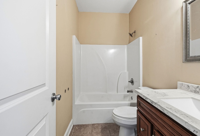 Bathroom featuring a white shower-tub combination, a vanity with a white countertop and integrated sink, a dark wood-finish vanity cabinet, a wall-mounted mirror with an ornate frame, and neutral wall paint