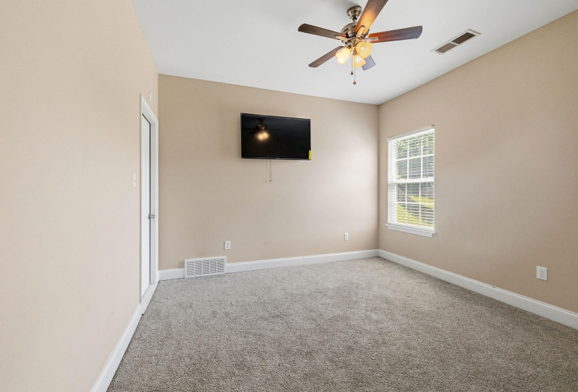 Carpeted room with a ceiling fan light fixture, mounted television, a window with blinds, and light-colored walls