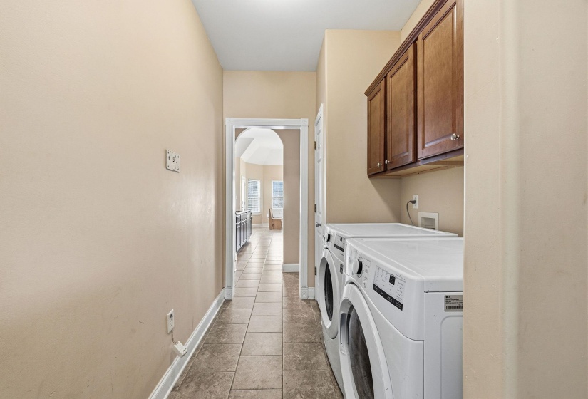 Dedicated laundry area featuring ceramic tile flooring, wood-finish cabinetry, and neutral wall tones