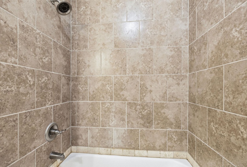 Bathtub with textured tile surround, complete with a shower head and coordinating bath fixtures