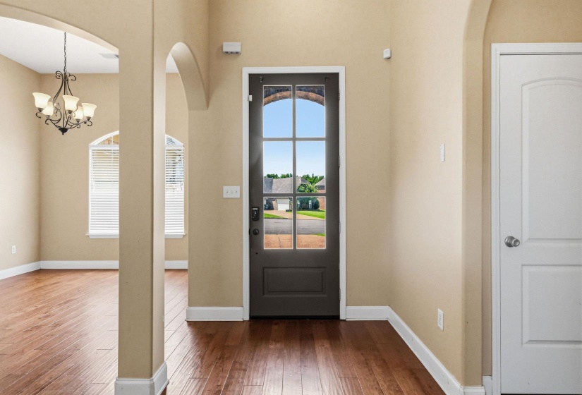 Entryway featuring wood-finish flooring, a dark-paneled door with upper window panes, and arched passages