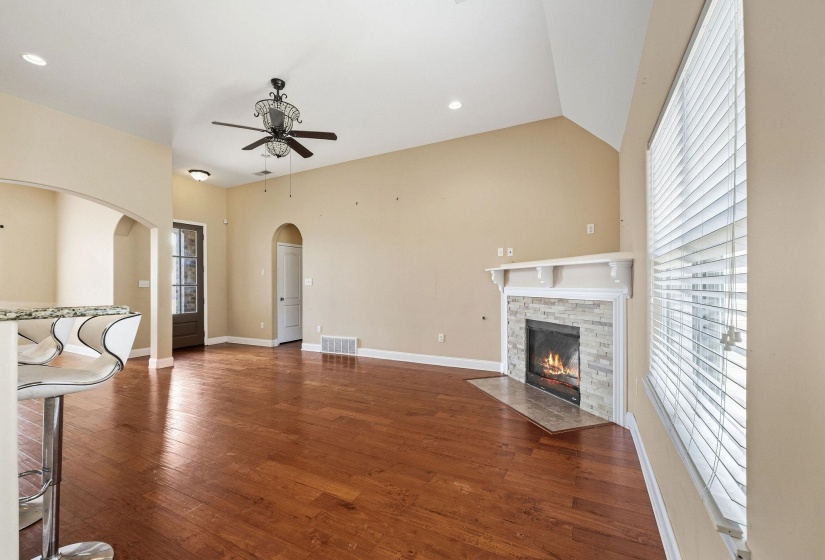 Spacious living area featuring wood-finish flooring, vaulted ceilings, and a corner fireplace with stone surround and white mantel