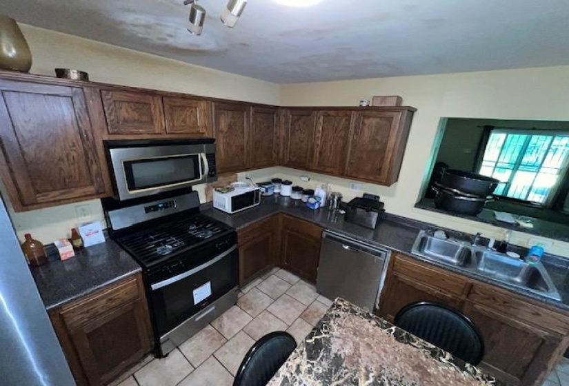 Kitchen featuring wood cabinetry, stainless steel appliances, dark countertops, and tiled flooring