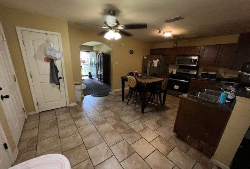 Kitchen featuring tile flooring, dark wood-finish cabinetry, stainless steel appliances, and an arched entryway