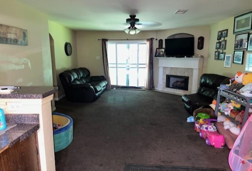 Living area featuring a corner fireplace with a white mantel and tile surround, sliding glass door access to an exterior space, an arched doorway, and an overhead ceiling fan