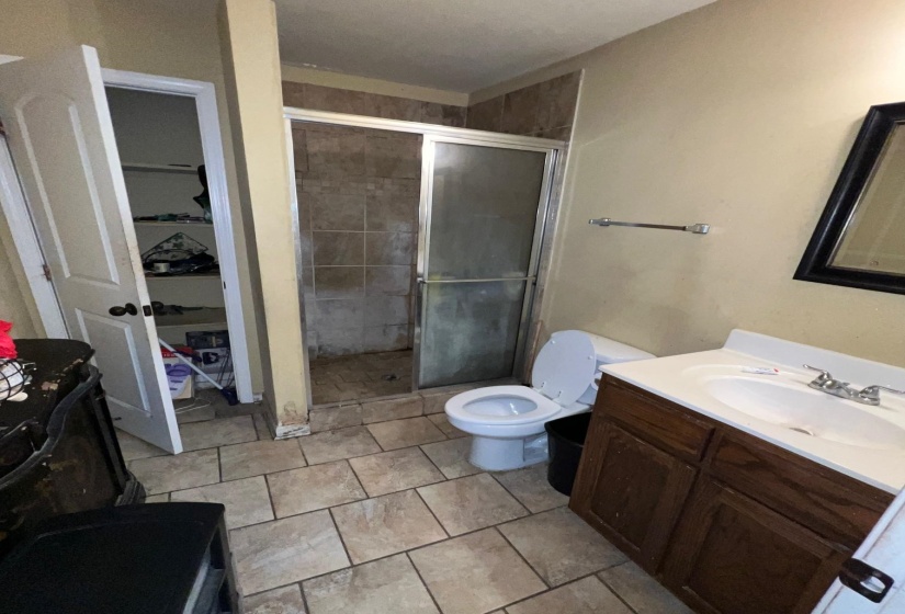 Bathroom featuring a glass-enclosed shower, single vanity with integrated sink, tile flooring, and a built-in storage closet