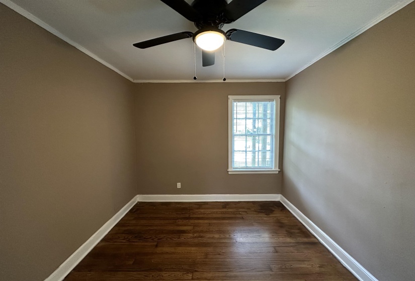 Room featuring wood-finish flooring, a single window with white trim, and a ceiling fan with integrated lighting