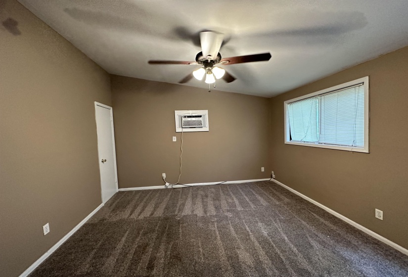 Carpeted room featuring a ceiling fan, window unit air conditioner, and a single window with blinds