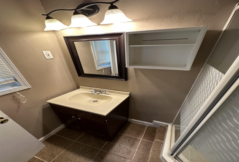 Bathroom vanity with integrated sink, framed mirror, and wall-mounted light fixture