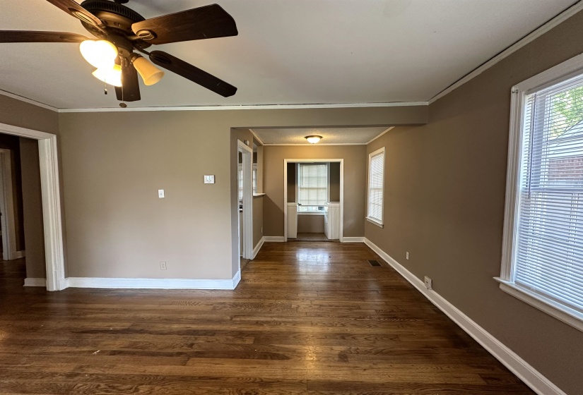 Expansive room featuring wood-finish flooring, neutral-toned walls, a ceiling fan with integrated lighting, and multiple windows with blinds