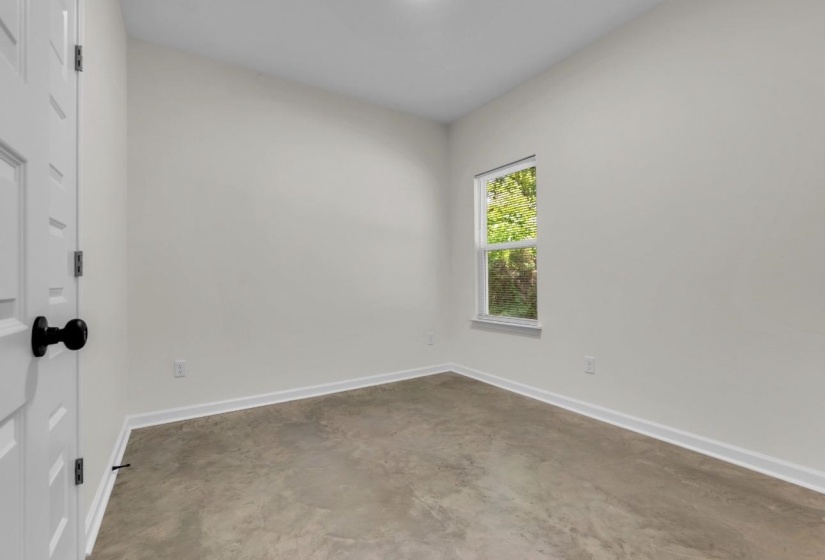 Neutral wall paint with white trim, a single window, and concrete flooring