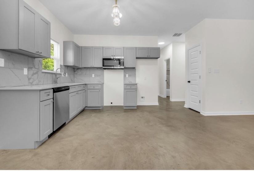 Modern kitchen featuring light gray cabinetry, stainless steel appliances, a white tile backsplash with gray veining, and a contemporary ceiling fixture