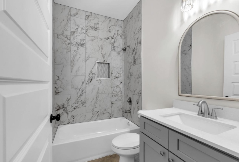 Bathroom featuring a white bathtub, marble-patterned tile surround with a recessed niche, and a gray vanity with a white countertop