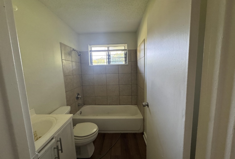 Bathroom featuring a tub and shower combination with tile surround, a window providing natural light, a white toilet, and a vanity with an integrated sink