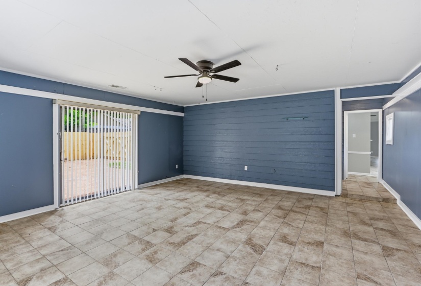 Spacious room featuring tile flooring, a sliding glass door with vertical blinds, and a dark blue accent wall with horizontal paneling
