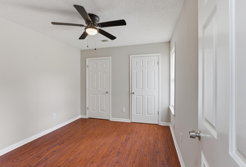 Room featuring wood-finish flooring, two paneled doors, a window with white trim, a textured ceiling, and a ceiling fan with integrated lighting