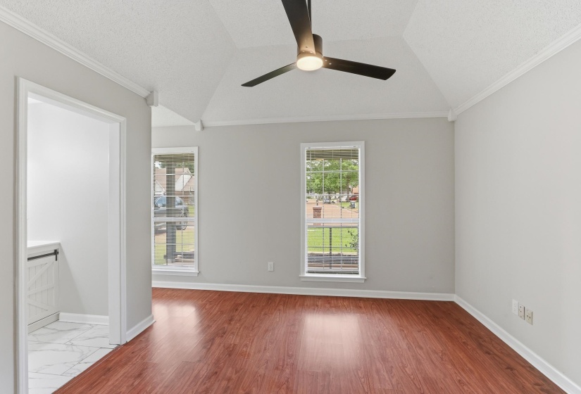 Vaulted ceiling room featuring wood-finish flooring, a ceiling fan with integrated lighting, and two framed windows