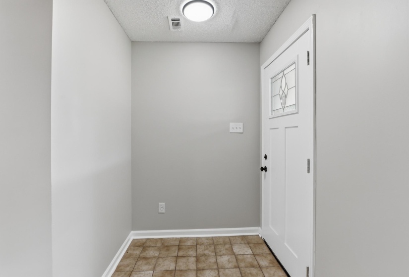Entryway featuring a white door with decorative glass inserts, matte black hardware, and an overhead flush-mount light fixture