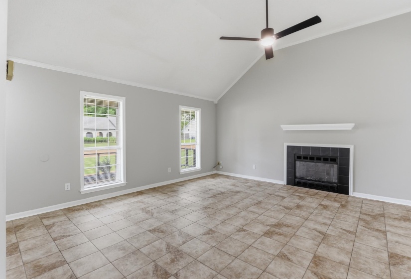 Living area featuring an angled vaulted ceiling, tile flooring, and a fireplace with a black tile surround and white mantel