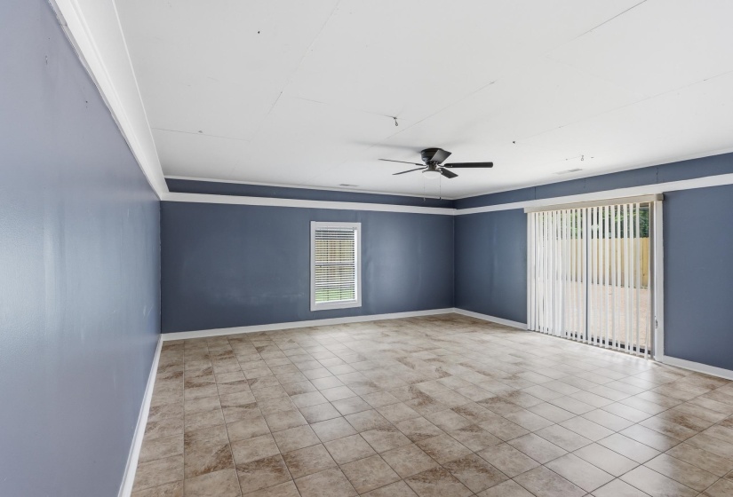 Spacious room featuring tile flooring, a window with blinds, sliding glass doors with vertical blinds, a ceiling fan, and crown molding